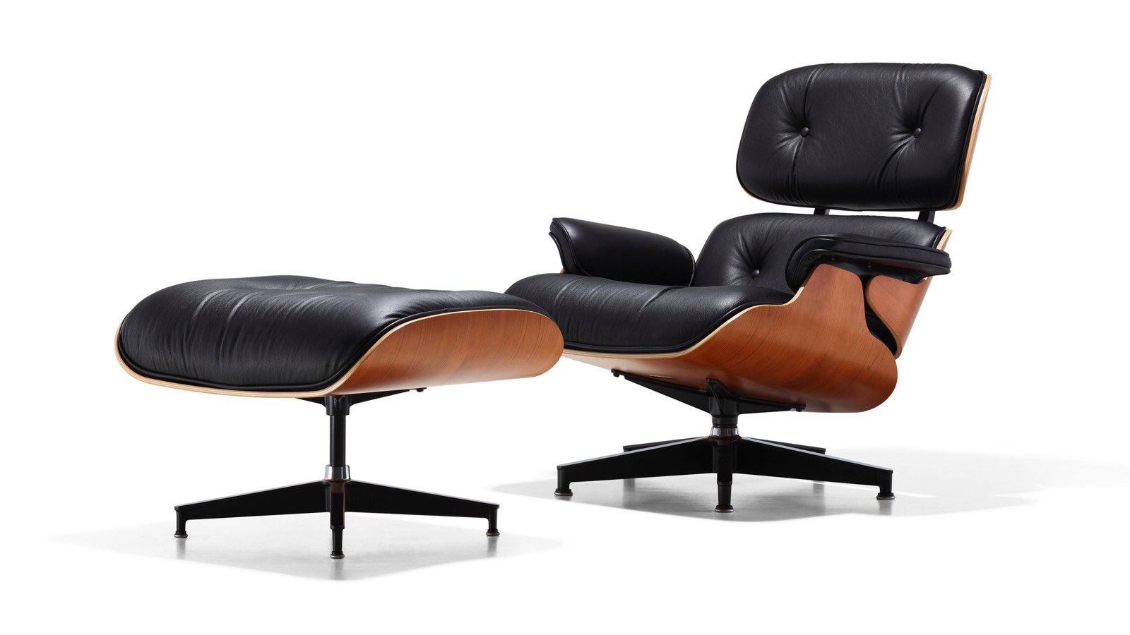 Black leather Eames Lounge Chair and Ottoman with a wood veneer shell, viewed from a 45-degree angle. Black leather Eames Lounge Chair and Ottoman with a wood veneer shell, viewed from a 45-degree angle.